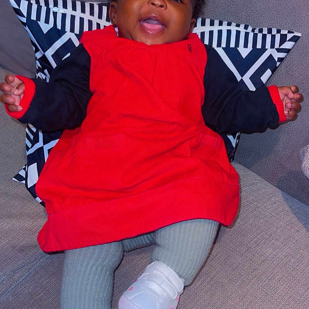 Kadiatou participe au concours pour gagner de l'argent avec cette photo : baby, black_hair, child, couch, cozy, cute, fabric, feet, happy, indoors, infant, legs, long_sleeves, patterned_pillow, pillow, pink_hearts, red_dress, seated, smiling, white_shoes