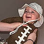 Hunter is registered to the contest to win money with this photo: baby, child, smiling, hat, onesie, football_design, hands, indoor, portrait, cute, happy, infant, skin, person, apparel, headwear, expression, holding, face, young