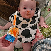 Hunter joined the competition — help win amazing prizes! baby, infant, bib, food, spoon, hand, quilt, blanket, bed, feeding, messy, orange_food, clothing, person, face, smile, socks, indoor, cute, child