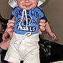 Hunter is registered to the contest to win money with this photo: baby, child, smiling, hat, white_hat, blue_shirt, royals, shorts, socks, nike_shoes, indoor, person, holding, cute, happy, face, legs, hands, infant, clothing