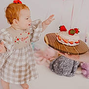 Eloise joined the competition — help win amazing prizes! baby, toddler, child, cake, strawberry, birthday, balloon, plush_toy, red_hair, dress, checkered, wooden_platter, celebration, curious, indoors, person, cute, smiling, decor, hand