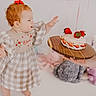 baby, toddler, child, cake, strawberry, birthday, balloon, plush_toy, red_hair, dress, checkered, wooden_platter, celebration, curious, indoors, person, cute, smiling, decor, hand