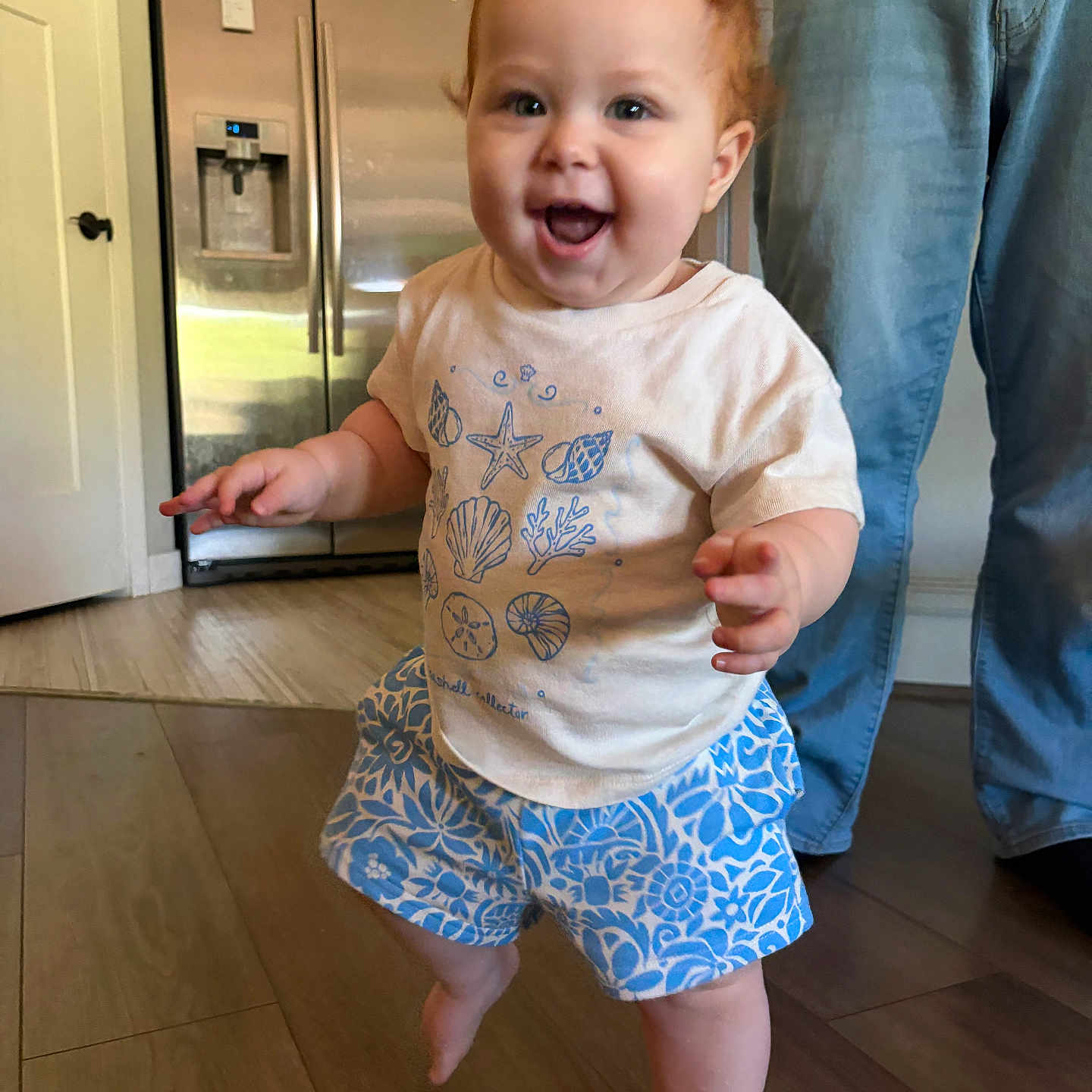 Eloise joined the competition — help win amazing prizes! toddler, child, indoor, smiling, walking, barefoot, tshirt, shorts, red_hair, person, floor, jeans, adult, home, refrigerator, cabinet, wooden_floor, happy, cute, family