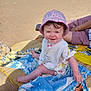 baby, child, beach, sand, towel, hat, pink_hat, bib, smile, sunny, sea, water, person, outdoor, summer, relaxation, vacation, clothing, happy, family