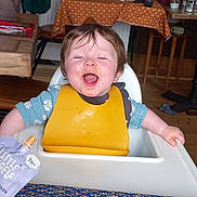 Elizabeth joined the competition — help win amazing prizes! baby, child, dining, expression, food, food_pouch, furniture, happy, high_chair, indoor, kitchen, messy_face, person, seat, smiling, spoon, tablecloth, toddler, wooden_chair, yellow_bib