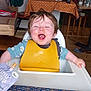 toddler, baby, high_chair, yellow_bib, messy_face, happy, smiling, food, spoon, food_pouch, tablecloth, kitchen, indoor, child, person, furniture, dining, wooden_chair, expression, seat