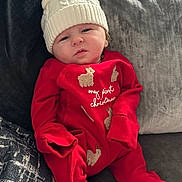 Teddy joined the competition — help win amazing prizes! baby, infant, red_onesie, knitted_hat, bear_ears, christmas_outfit, couch, pillow, cozy, cute, child, holiday, festive, soft_fabric, indoors, portrait, smiling, sitting, warm, relaxed
