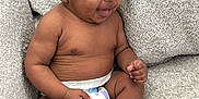 Braxton is registered to the contest to win money with this photo: baby, smiling, diaper, curly_hair, sitting, couch, indoor, child, cute, infant, happy, skin, person, portrait, toddler, expression, relaxed, comfort, young, furniture