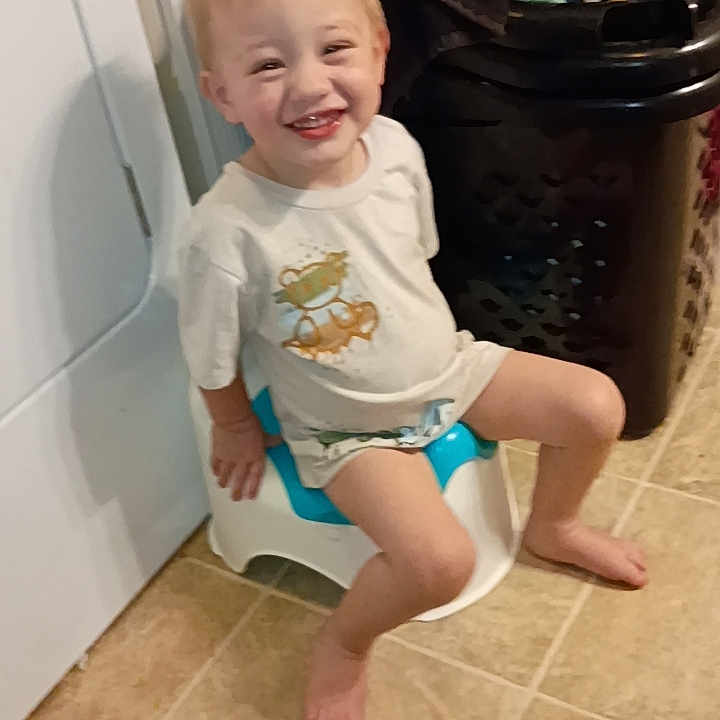 Axil is registered to the contest to win money with this photo: toddler, child, smiling, potty, bathroom, tile_floor, laundry_basket, towels, shorts, shirt, light_hair, happy, indoor, footwearless, home, cute, young_child, sitting, childcare, playful