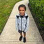 Brandon joined the competition — help win amazing prizes! child, sidewalk, outdoor, grass, bushes, person, jacket, shorts, sneakers, black_shoes, gray_jacket, braided_hair, casual_clothing, daylight, walking_path, greenery, portrait, young, standing, nature