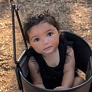 Braelynn is registered to the contest to win money with this photo: toddler, child, swing, playground, outdoor, black_clothing, curly_hair, face, eyes, seat, wood_chips, daylight, park, baby, infant, person, cute, young_child, nature, resting