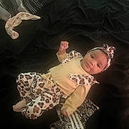 Braelynn joined the competition — help win amazing prizes! baby, infant, child, yellow_clothing, leopard_print, headband, blanket, lying_down, cute, portrait, indoor, socks, raised_fist, comfortable, soft_lighting, young_child, fashion, cozy, adorable, looking_at_camera