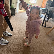 Braelynn is registered to the contest to win money with this photo: toddler, child, indoor, carpet, walking, hand_holding, vacuum_cleaner, adult, pink_clothing, curly_hair, sneakers, window, living_room, plant, furniture, toy, cabinet, table, chair, smiling