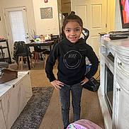 Serenity is registered to the contest to win money with this photo: child, smiling, indoor, black_hoodie, jeans, carpet, backpack, living_room, television, table, chair, door, rug, person, furniture, home, bag, happy, standing, casual