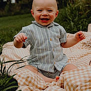 Riker joined the competition — help win amazing prizes! baby, blanket, casual_clothing, child, cute, daytime, face, grass, greenery, happy, infant, nature, one_person, outdoor, portrait, sitting, smiling, striped_shirt, sunlight, young