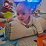 baby, infant, pillow, play_mat, cat, television, woman, living_room, floor, toy, colorful, curious, face, hand, clothing, indoor, carpet, smile, person, couch