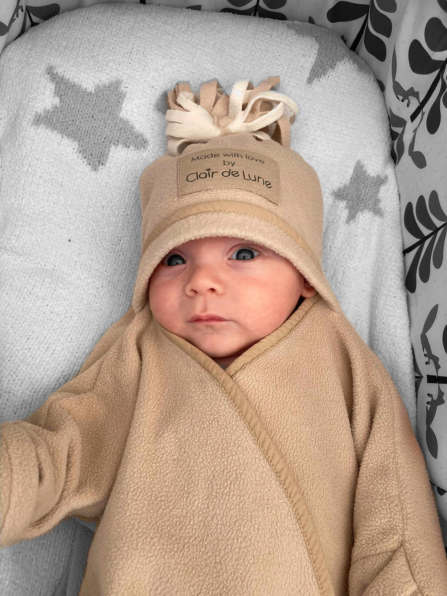 Archie is registered to the contest to win money with this photo: baby, infant, face, hat, fleece, blanket, star_pattern, blue_eyes, clothing, cute, newborn, portrait, soft_texture, wrapped, lying_down, indoor, warm, adorable, child, cozy