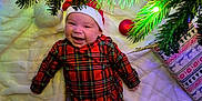 Jasper is registered to the contest to win money with this photo: baby, blanket, christmas_lights, christmas_tree, cozy, cute, decorations, feet, festive, greenery, happy, holiday, indoors, infant, ornament, plaid_clothing, red, santa_hat, smiling, white