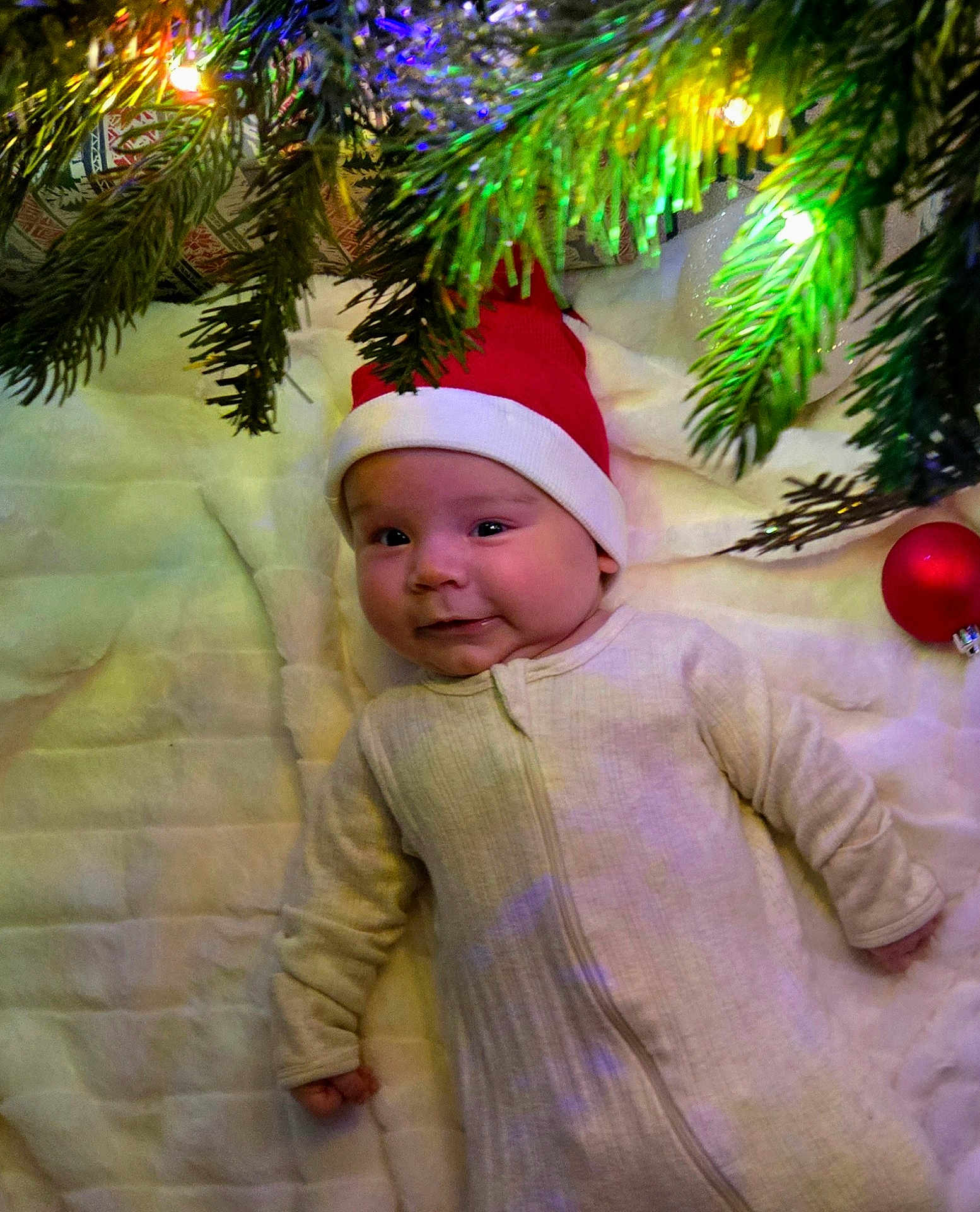 Jasper joined the competition — help win amazing prizes! baby, infant, santa_hat, christmas_tree, christmas_lights, ornament, blanket, holiday, festive, smile, face, child, cozy, indoors, celebration, cute, headwear, red, green, winter