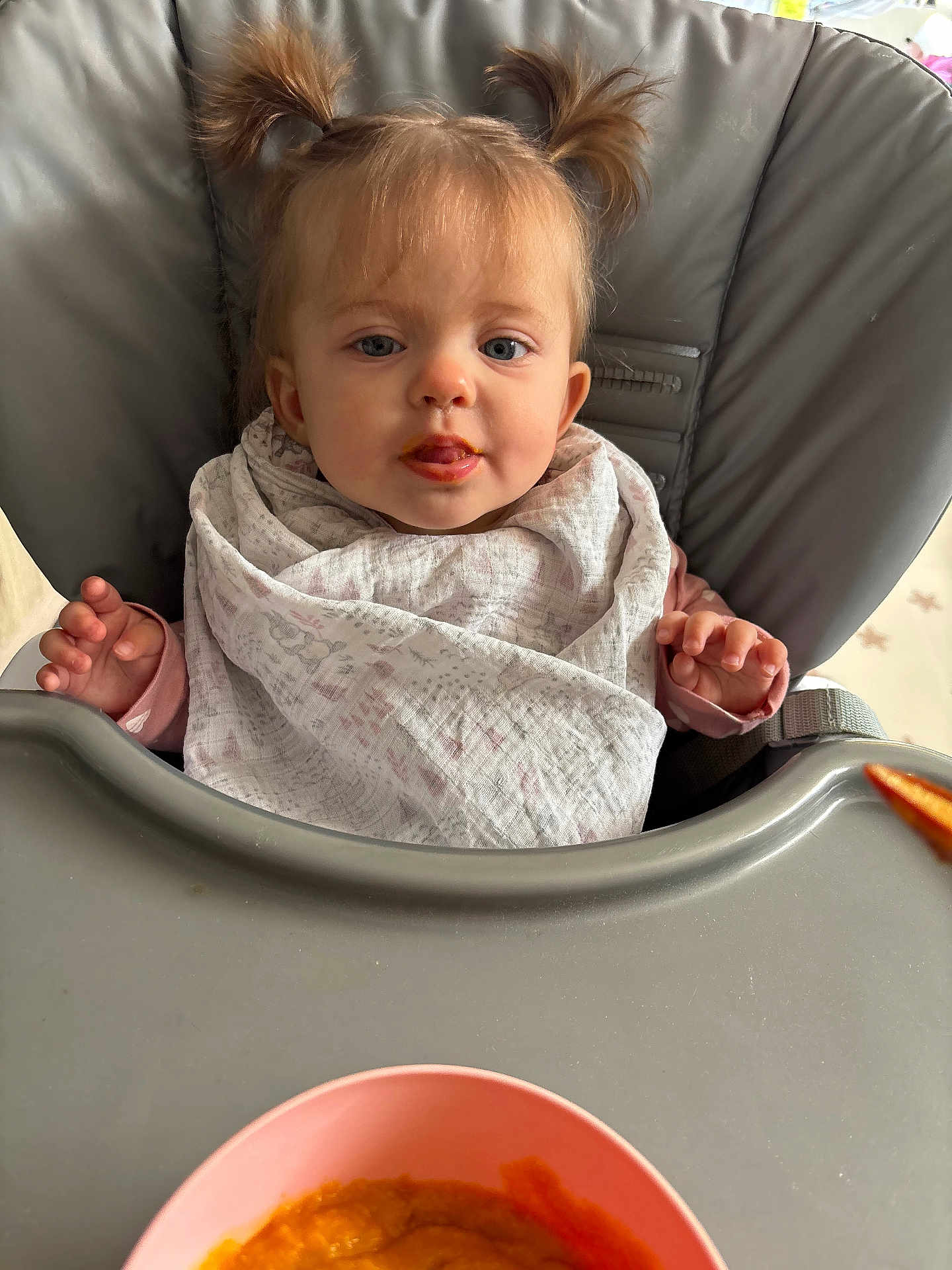 Alma a rejoint le concours — aidez-le/la à gagner de superbes lots ! baby, child, high_chair, bib, pigtails, food, baby_food, orange_puree, face, blue_eyes, hands, feeding_time, indoor, cute, infant, meal, smudge, pink_bowl, table, curious