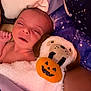 newborn, baby, infant, sleepy, blanket, plush_toy, halloween, pumpkin, dog_face, bed, bedding, galaxy_pattern, cozy, resting, child, soft_toy, cute, indoor, portrait, closeup