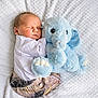 baby, bed, blue_elephant, clothing, cozy, cuddle, indoor, infant, infant_clothing, newborn, nursery, peaceful, plush_toy, portrait, sleeping, small_child, soft_texture, stuffed_elephant, top_view, white_blanket