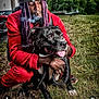 man, dog, outdoor, grass, smoke, cigar, beanie, purple_hair, dreadlocks, red_clothing, tongue_out, pet, leash, trees, cloudy_sky, trailer, motorcycle, hand, kneeling, portrait