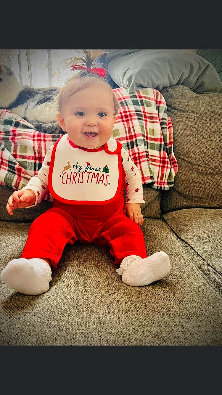 Remy is registered to the contest to win money with this photo: baby, baby_toddler_clothing, carmine, child, christmas, couch, eye, floor, flooring, happy, pattern, person, pillow, plaid, sitting, sleeve, smile, sock, t_shirt, tartan