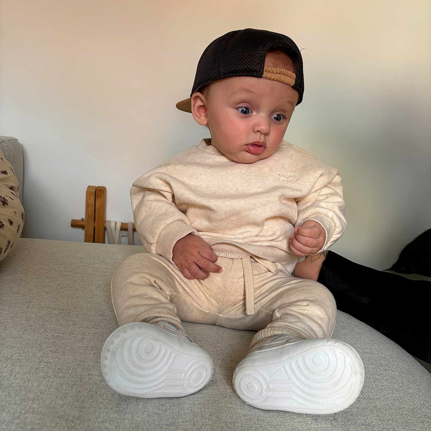 Sacha a rejoint le concours — aidez-le/la à gagner de superbes lots ! baby, cap, child, clothing, couch, curious, face, footwear, furniture, indoor, neutral_background, person, portrait, shoes, sitting, sweatpants, sweatshirt, white_shoes, wide_eyes, young_child