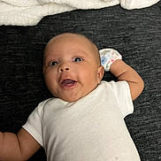 Mo Zyiah joined the competition — help win amazing prizes! baby, infant, smiling, white_onesie, mittens, blanket, lying_down, dark_background, happy, face, cute, child, newborn, skin, head, arms, person, indoors, expression, young