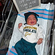 Stormi joined the competition — help win amazing prizes! newborn, baby, infant, hospital, bassinet, smiling, clothing, hat, blanket, sign, text, sleepwear, cute, child, portrait, indoors, resting, person, happy, newborn_baby