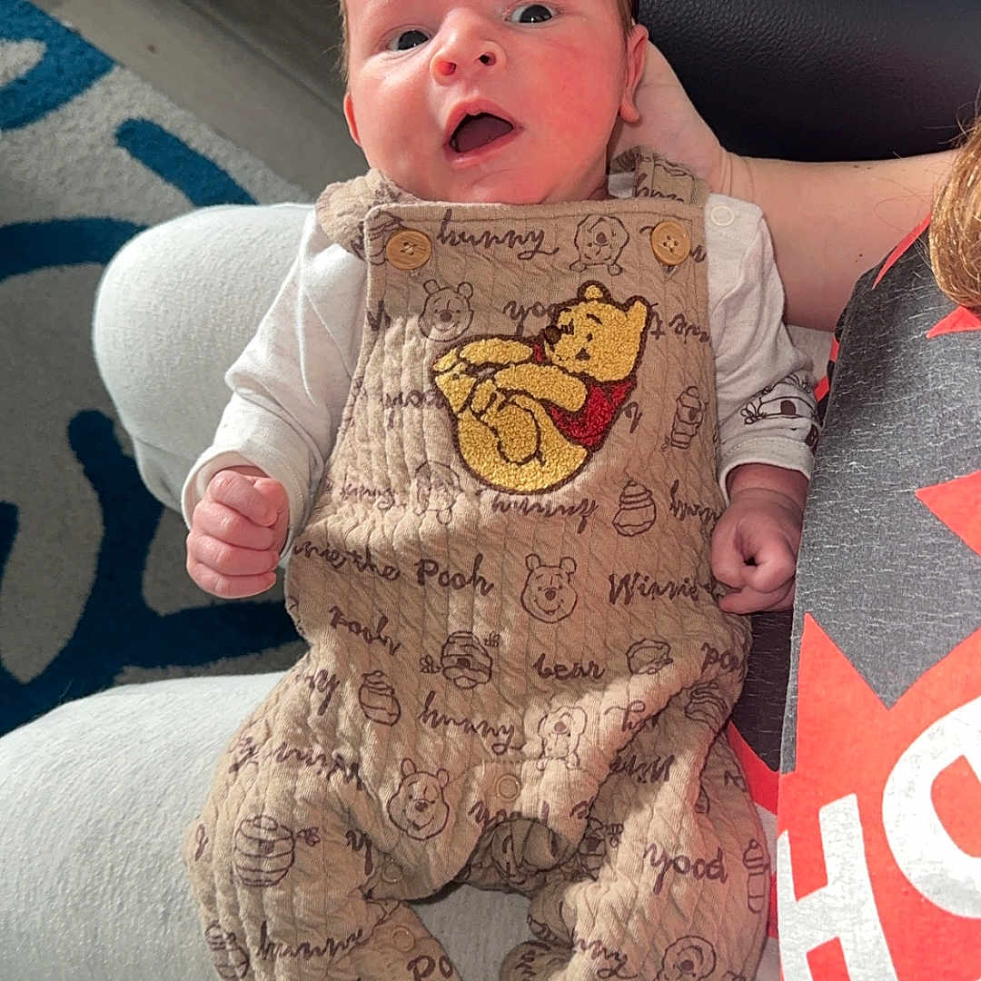 Devlin joined the competition — help win amazing prizes! adult_partial, arm, baby, blanket, couch, cute, face, floor, hand, indoor, infant, onesie, open_mouth, overalls, portrait, rug, socks, striped_socks, wide_eyes, winnie_the_pooh