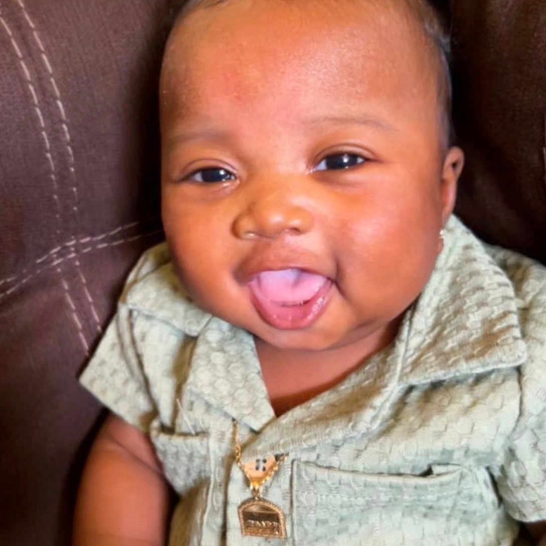 Jaliq is registered to the contest to win money with this photo: baby, brown_furniture, buttoned_shirt, child, couch, curly_hair, cute, face, green_clothing, hand, happy, indoors, infant, necklace, portrait, sitting, skin, smiling, tongue_out, young_child