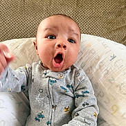 Javari is registered to the contest to win money with this photo: adorable, baby, bedding, big_eyes, closeup, clothing, couch, cozy, cute, facial_expression, hand, indoor, infant, knit_texture, mouth_open, onesie, pillow, portrait, sitting, surprised