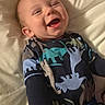 baby, infant, child, smiling, laughing, portrait, face, bed, bedding, indoors, cozy, pajamas, dinosaur_pattern, clothing, happy, lying_down, close_up, warm_lighting, brown_hair, home