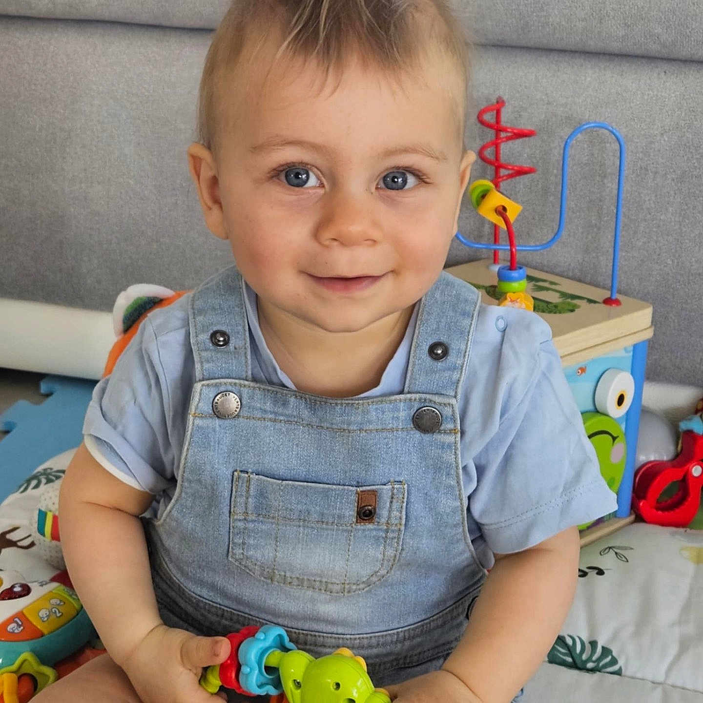 Ethan a rejoint le concours — aidez-le/la à gagner de superbes lots ! baby, blue_eyes, child, colorful, cute, denim, face, hand, happy, indoor, mohawk, overalls, person, playmat, playtime, shirt, sitting, smiling, toddler, toy