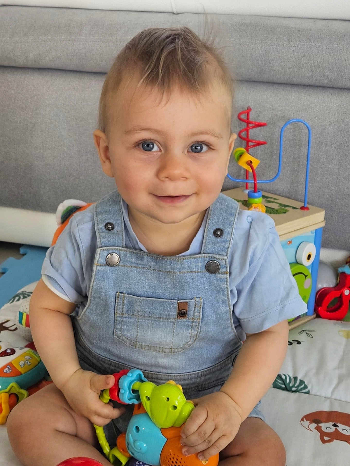 Ethan a rejoint le concours — aidez-le/la à gagner de superbes lots ! toddler, child, smiling, blue_eyes, mohawk, overalls, denim, toy, colorful, indoor, playmat, cute, happy, person, baby, sitting, hand, face, shirt, playtime