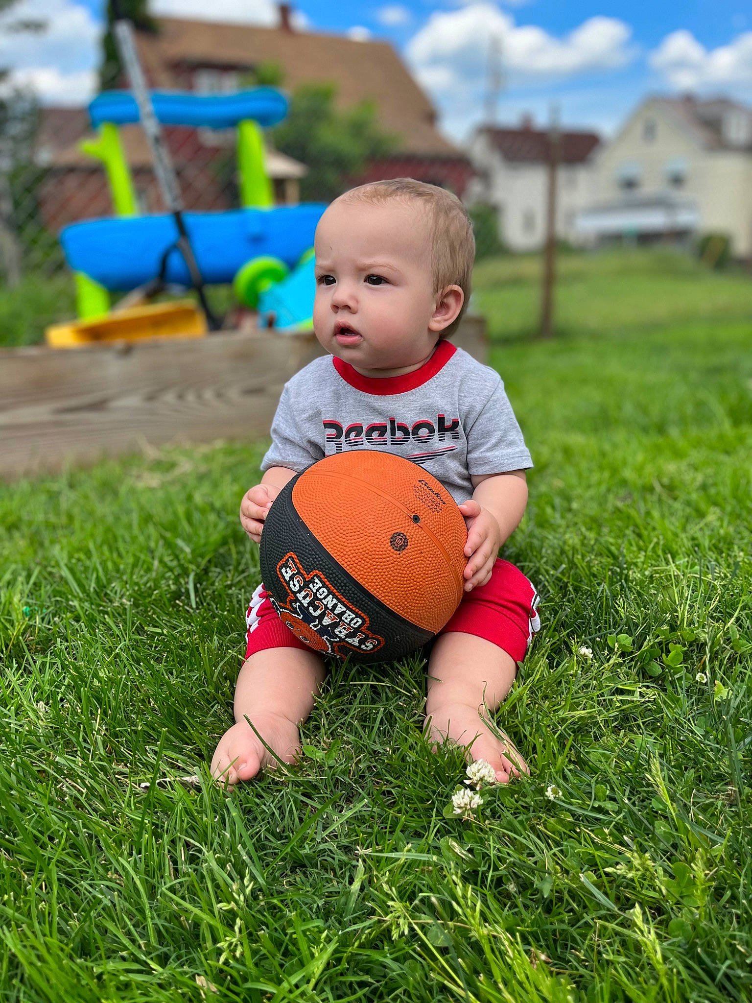 Ty is registered to the contest to win money with this photo: baby, ball, blue, cloud, football, fun, grass, grassland, happy, leisure, people_in_nature, person, plant, player, playing_with_kids, skin, sky, sneakers, sports_equipment, sunlight