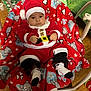 baby, christmas, santa_claus_costume, blanket, teddy_bear_pattern, holiday, festive, red, white, black, infant, cute, indoors, floor, wooden_floor, socks, hat, present, chair, face