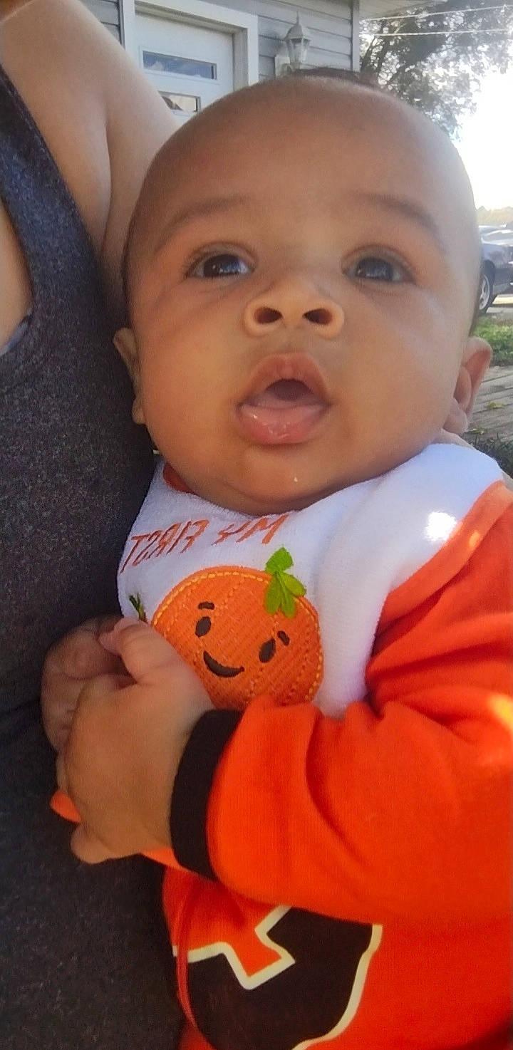 Judson is registered to the contest to win money with this photo: baby, baby_toddler_clothing, bib, cheek, child, eyebrow, eyelash, finger, happy, iris, lip, mouth, neck, nose, orange, outerwear, person, plant, skin, toddler