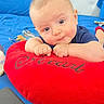 Liam Alexander joined the competition — help win amazing prizes! baby, infant, child, portrait, face, smiling, curious, indoor, cushion, red_cushion, blue_bedding, toy, sitting, lying_down, short_hair, blue_shirt, red_clothing, close_up, home, photography