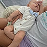 Liam Alexander is registered to the contest to win money with this photo: baby, infant, sleeping, portrait, indoors, white_romper, bow_tie, pacifier, blanket, bassinet, adult, parent, arms, cozy, home, soft_lighting, close_up, relaxed, family, nap