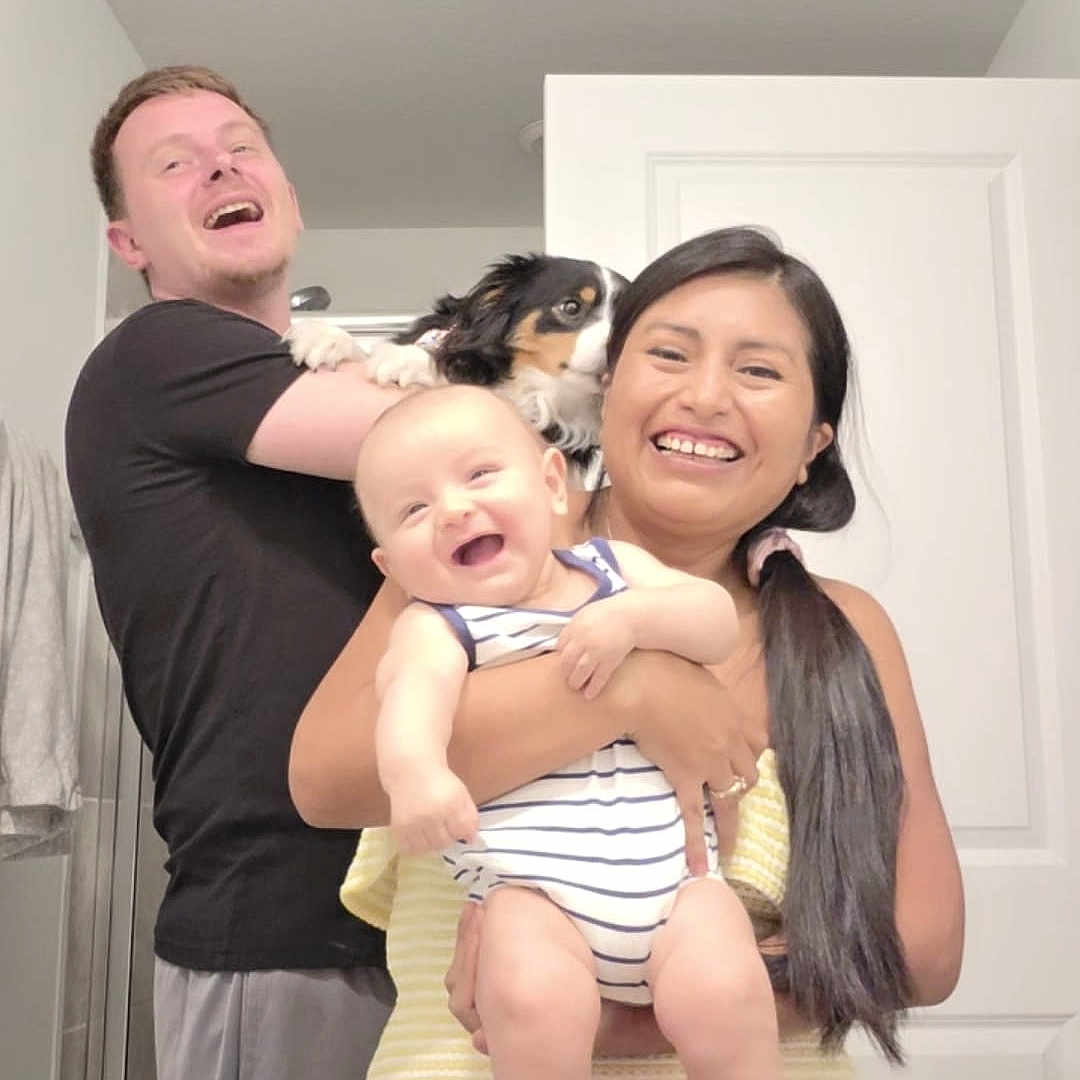 Liam Alexander joined the competition — help win amazing prizes! baby, child, infant, family, parents, adults, smiling, laughing, portrait, indoor, bathroom, doorway, dog, pet, holding, striped_clothing, yellow_blanket, home, happy, group_photo