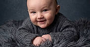Jeremiah is registered to the contest to win money with this photo: baby, infant, smile, face, portrait, knit_sweater, fluffy_blanket, cozy, cute, child, soft_texture, head, hands, expression, warm_clothing, indoor, studio, photography, blue_background, young