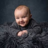 baby, infant, smile, face, portrait, knit_sweater, fluffy_blanket, cozy, cute, child, soft_texture, head, hands, expression, warm_clothing, indoor, studio, photography, blue_background, young