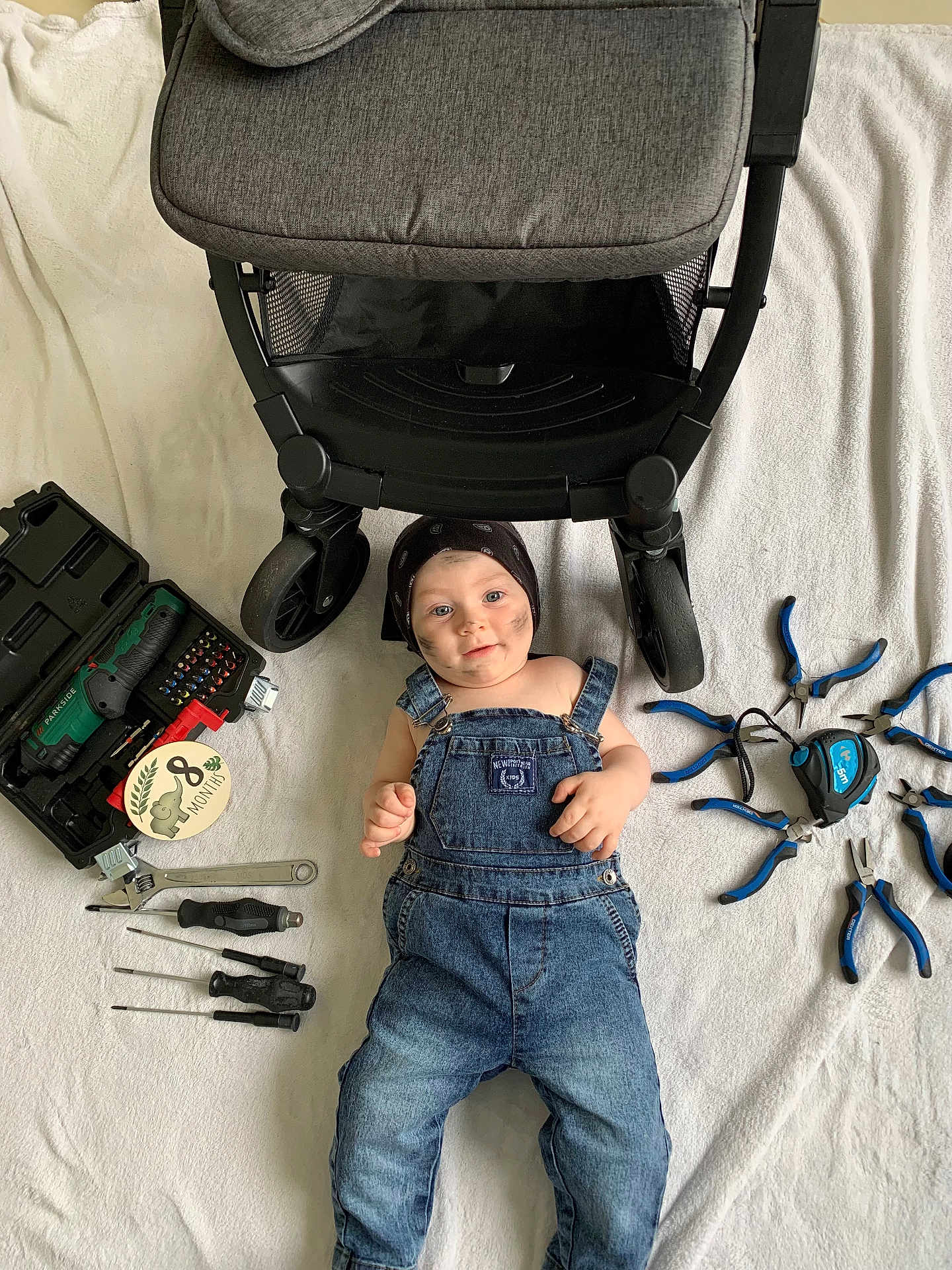 Loris a rejoint le concours — aidez-le/la à gagner de superbes lots ! baby, denim_overalls, bandana, tools, stroller, white_blanket, face, smudged_face, pliers, screwdrivers, wrench, measuring_tape, toolbox, lying_down, indoors, child, cute, blue_jeans, happy, portrait
