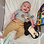 baby, infant, smiling, toy, plush_toy, penguin, crib, blanket, clothing, pants, onesie, child, happy, face, person, indoor, colorful, soft, playful, cute
