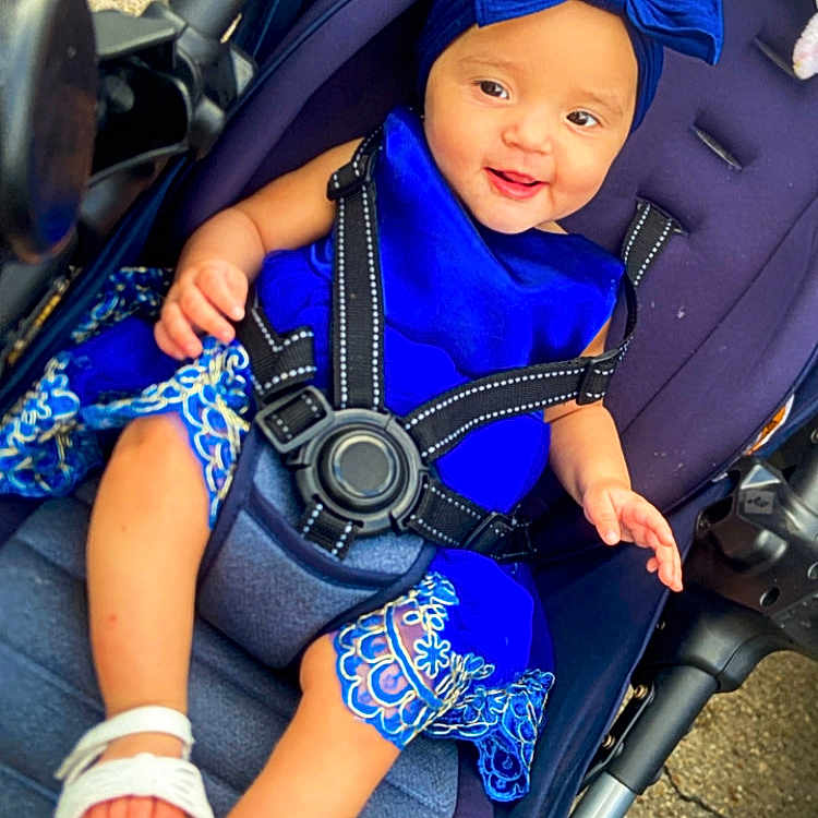 Dianellyz Anaia joined the competition — help win amazing prizes! accessory, baby, blue_dress, child, cute, daylight, fabric, footwear, happy, headband, infant, outdoor, pattern, person, sandal, seatbelt, sitting, skin, smiling, stroller
