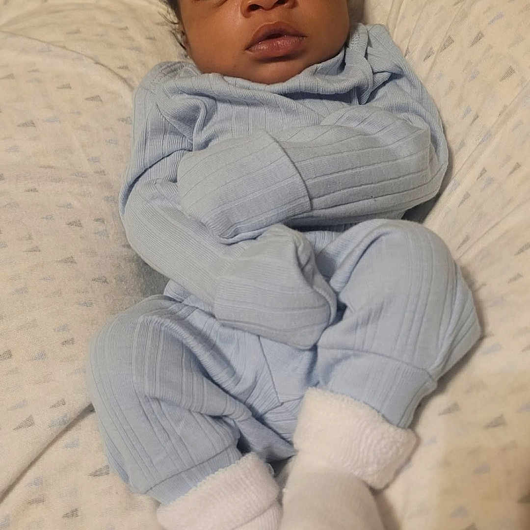 Zacharias is registered to the contest to win money with this photo: baby, blanket, blue_clothing, child, cozy, cute, face, feet, hands, head, indoors, infant, newborn, pajamas, peaceful, portrait, resting, sleeping, socks, soft_lighting