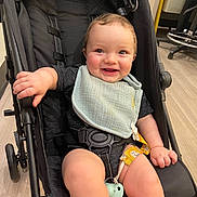 Jaxxon joined the competition — help win amazing prizes! baby, stroller, bib, smiling, happy, child, indoor, floor, black_stroller, pacifier, clothing, seatbelt, legs, hand, face, cute, infant, sitting, wooden_floor, toy